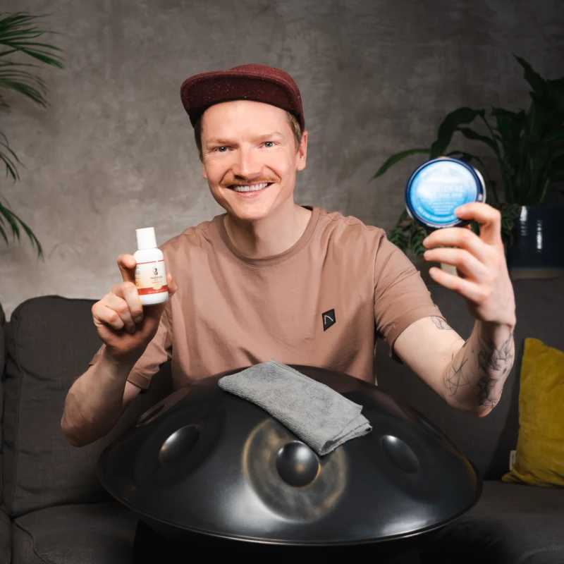 Handpan Pflege - Mann mit Handpan auf dem Schoß und Pflegeprodukten zur Handpan Pflege in den Händen