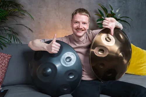 Handpan Test - Mann sitzt mit Handpan auf der Couch und zeigt einen Daumen nach oben und den anderen nach unten